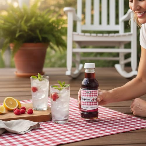 Woman holding Raspberry Iced Tea bottle on a porch with iced glasses, fresh raspberries, and lemons on a red gingham cloth.